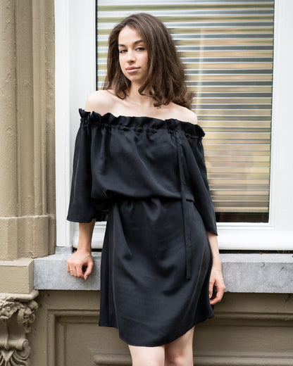 Model draagt zwart / antraciet zijden jurk No.6 van OAXO, off-shoulder gestyled.